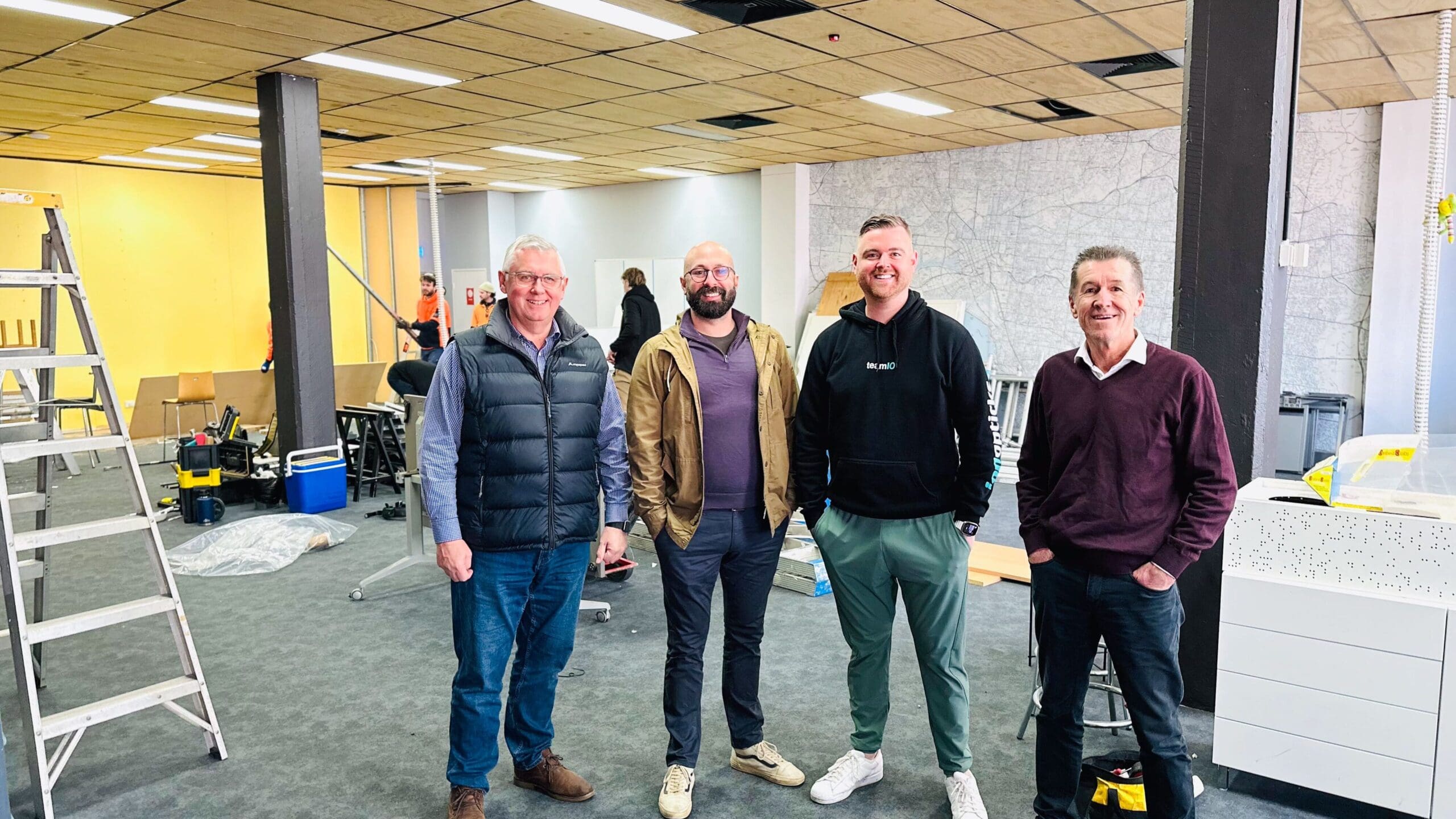 Four people standing in a row in front of a construction site as IonOpticks builds new facility in Melbourne. From left to right, Property and Facilities Project Manager, David Sinden; Managing Director, Xavier Perronnet; Head of Brand, Michael Sinden; Managing Director, Challenge Group, David Murphy.